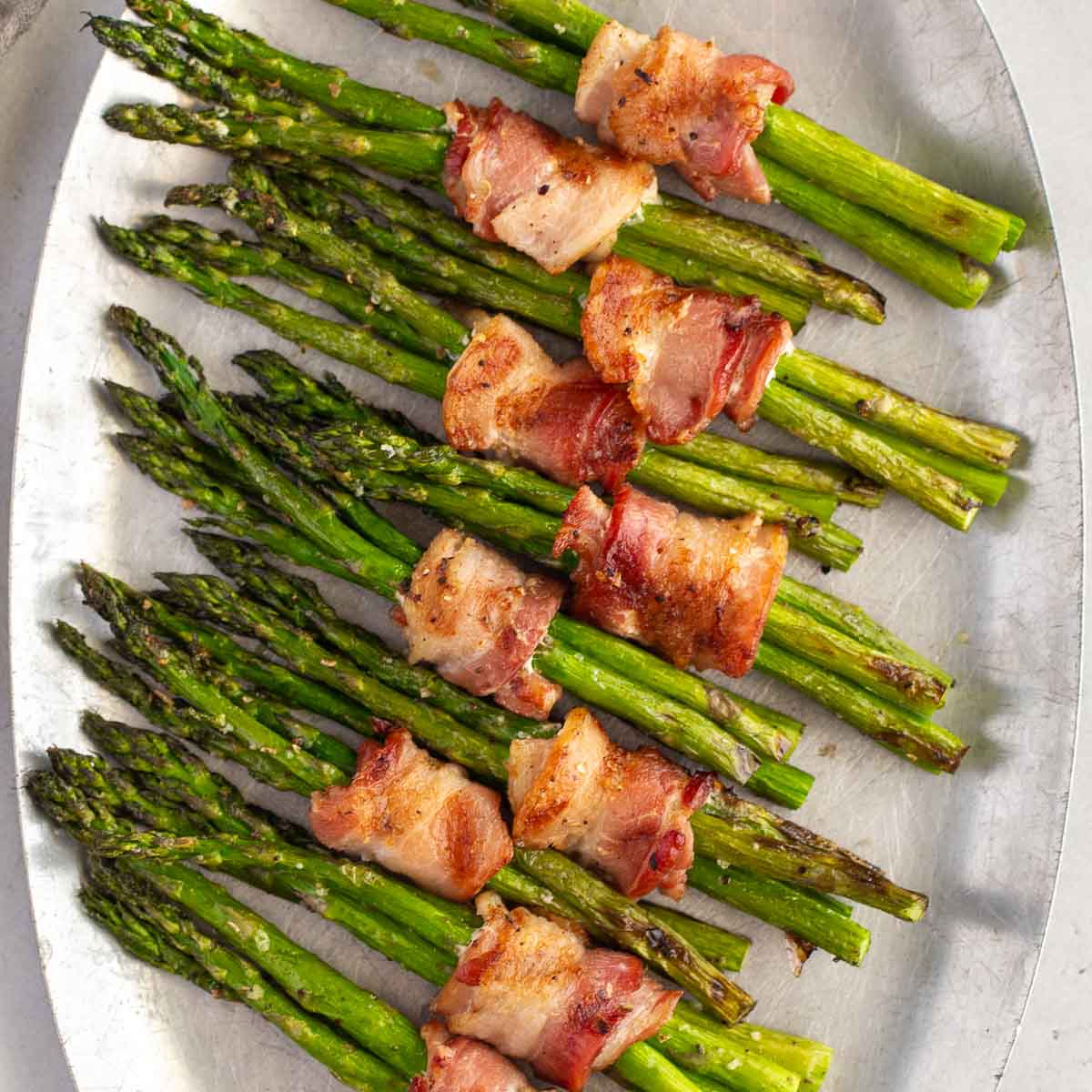 Bacon wrapped asparagus laid out on a metal serving tray.