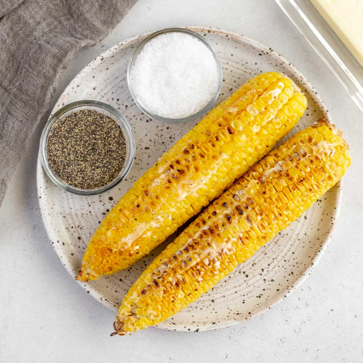 A speckled plate holding two pieces of corn on the cob with salt and pepper beside them.