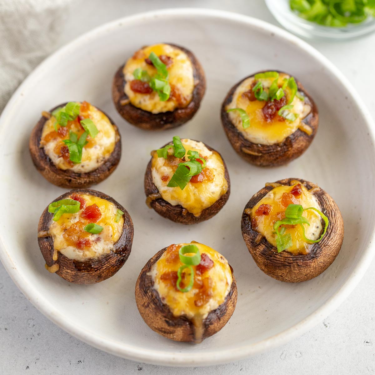 A white plate holding several grilled stuffed mushrooms.
