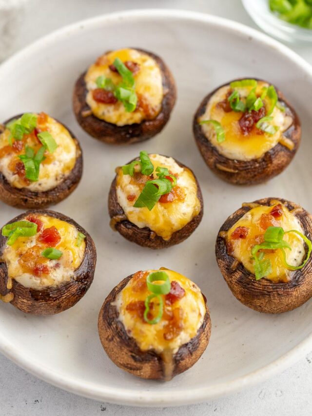 A white plate holding several grilled stuffed mushrooms.