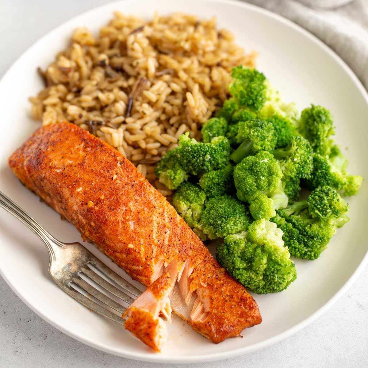 A piece of salmon on a white plate with sides of rice and broccoli.