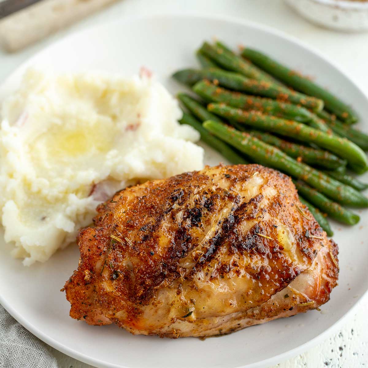 A grilled chicken breast on a white plate with mashed potatoes and green beans.