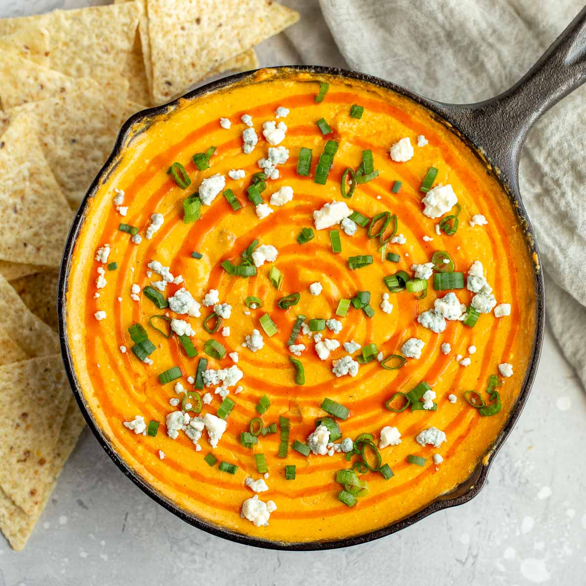 An overhead image of buffalo chicken dip in a cast iron skillet topped with green onions and blue cheese crumbles.
