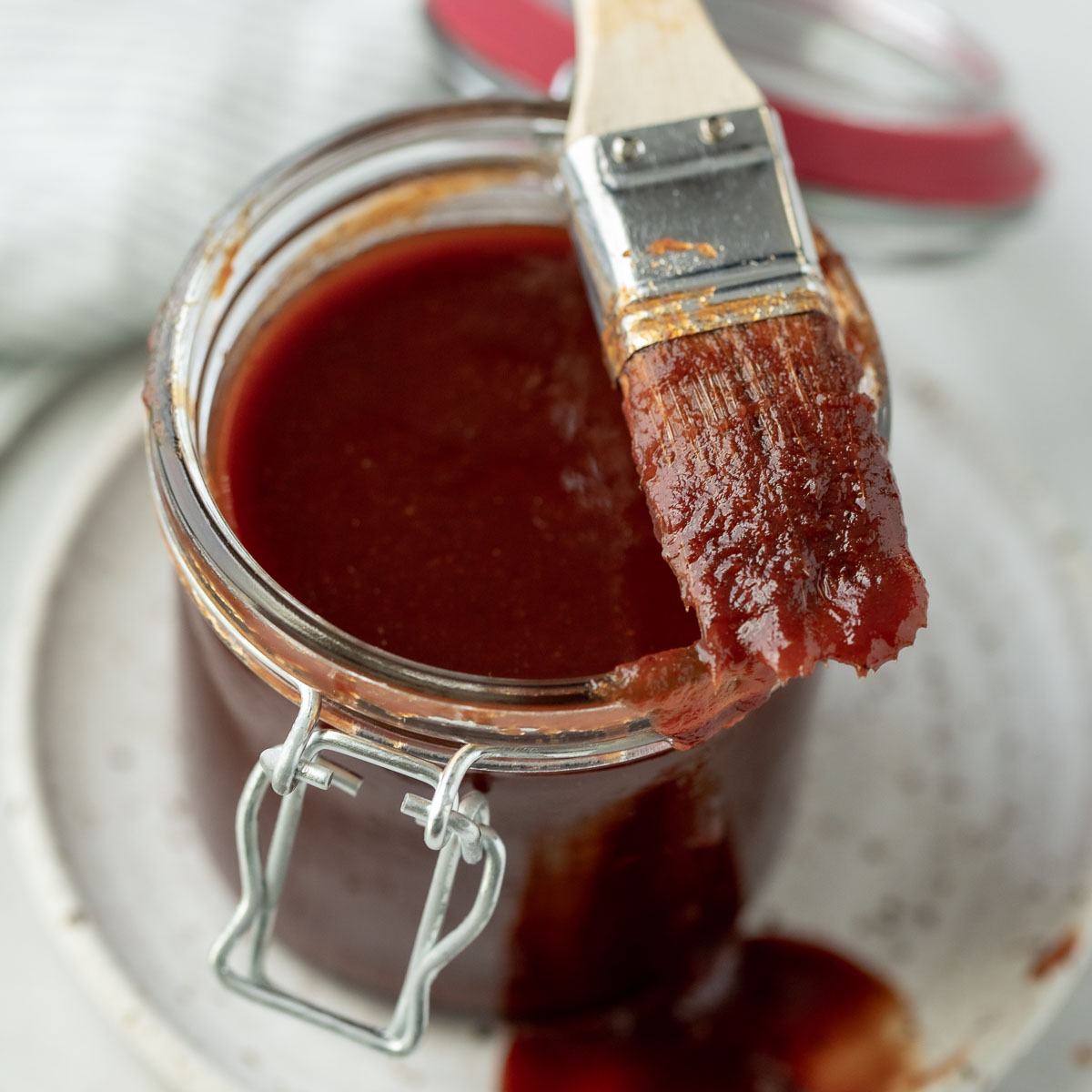 A basting brush covered in sauce resting on top a glass jar.