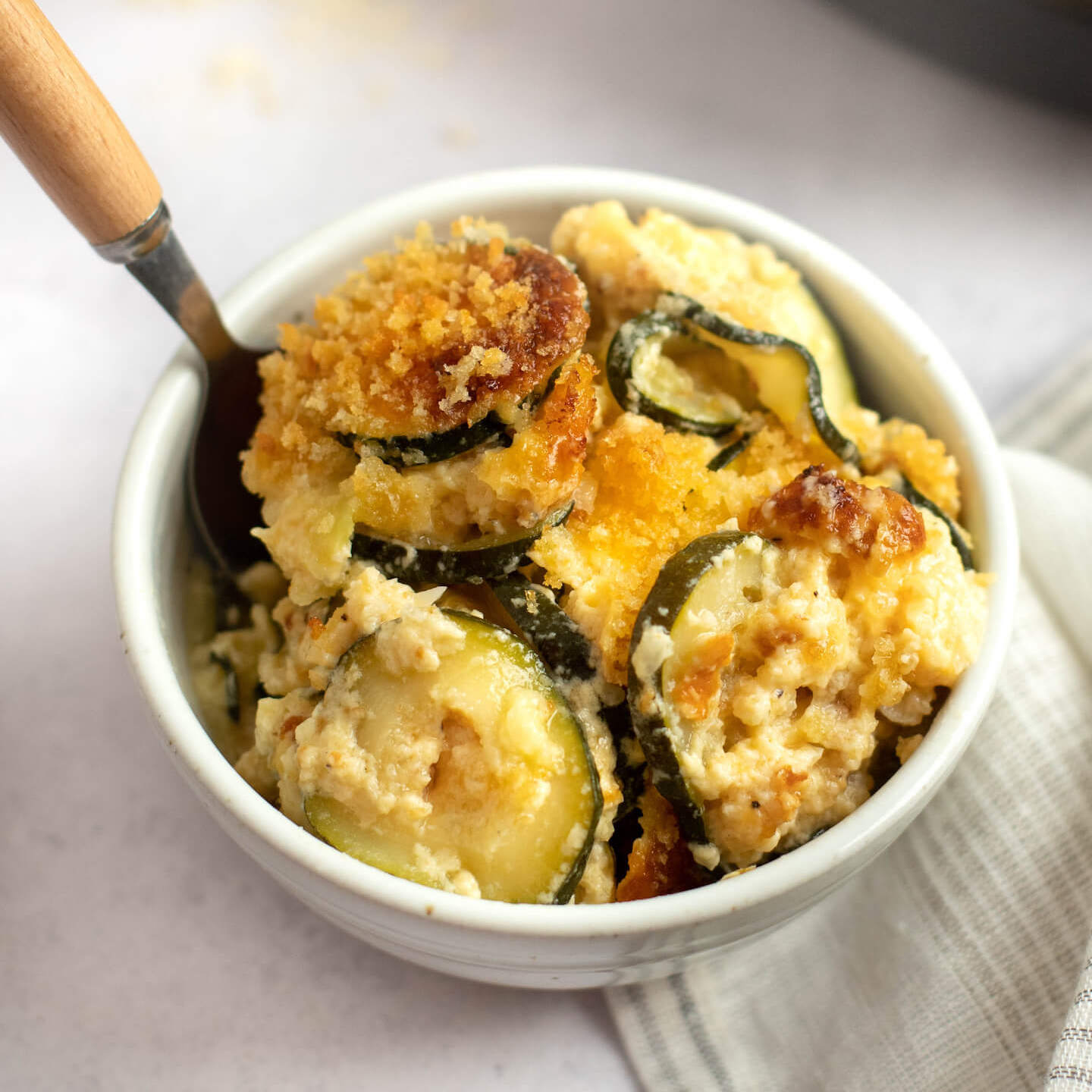 Zucchini casserole in a small white bowl with a fork on the side.